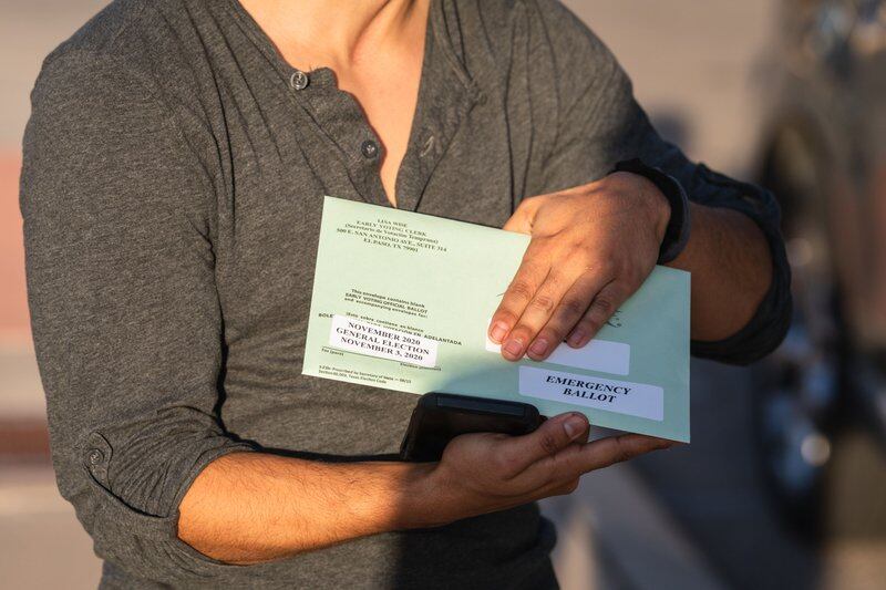 A person holds a green ballot envelope that reads “November 2020 election” and “emergency ballot.”