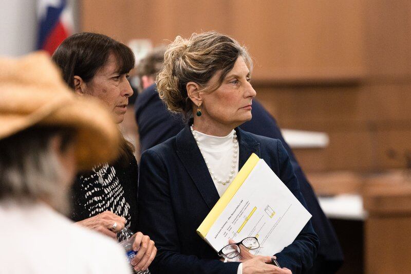 Two women sitting next to each other inside a courtroom face the judge’s bench.